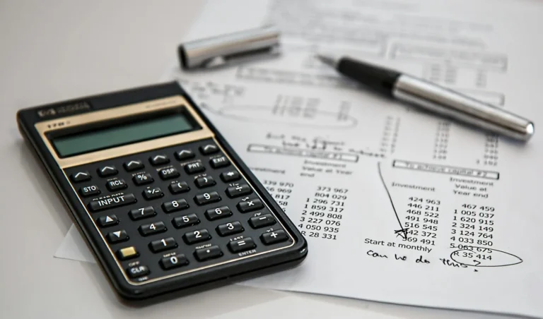 Calculadora científica e caneta sobre planilha com cálculos financeiros e anotações, representando atividades de orçamento e planejamento de obras.