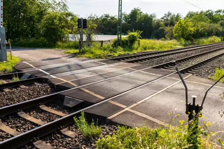 Imagem de uma passagem em nível ferroviária com pavimento polimérico modular, destacando a integração entre trilhos e via asfaltada em área arborizada.